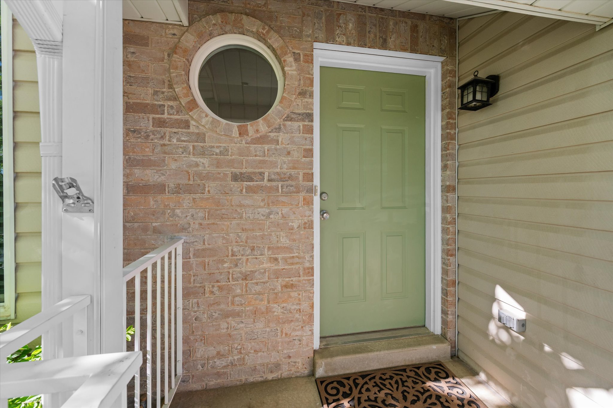 Entryway featuring a panel door, brick facade, circular window, and exterior wall sconce