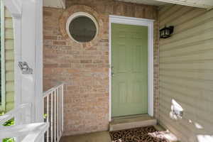 Entryway featuring a panel door, brick facade, circular window, and exterior wall sconce