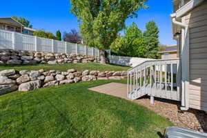 Lawn area featuring multiple natural stone retaining walls, a white vinyl fence, and a wooden deck with stairs