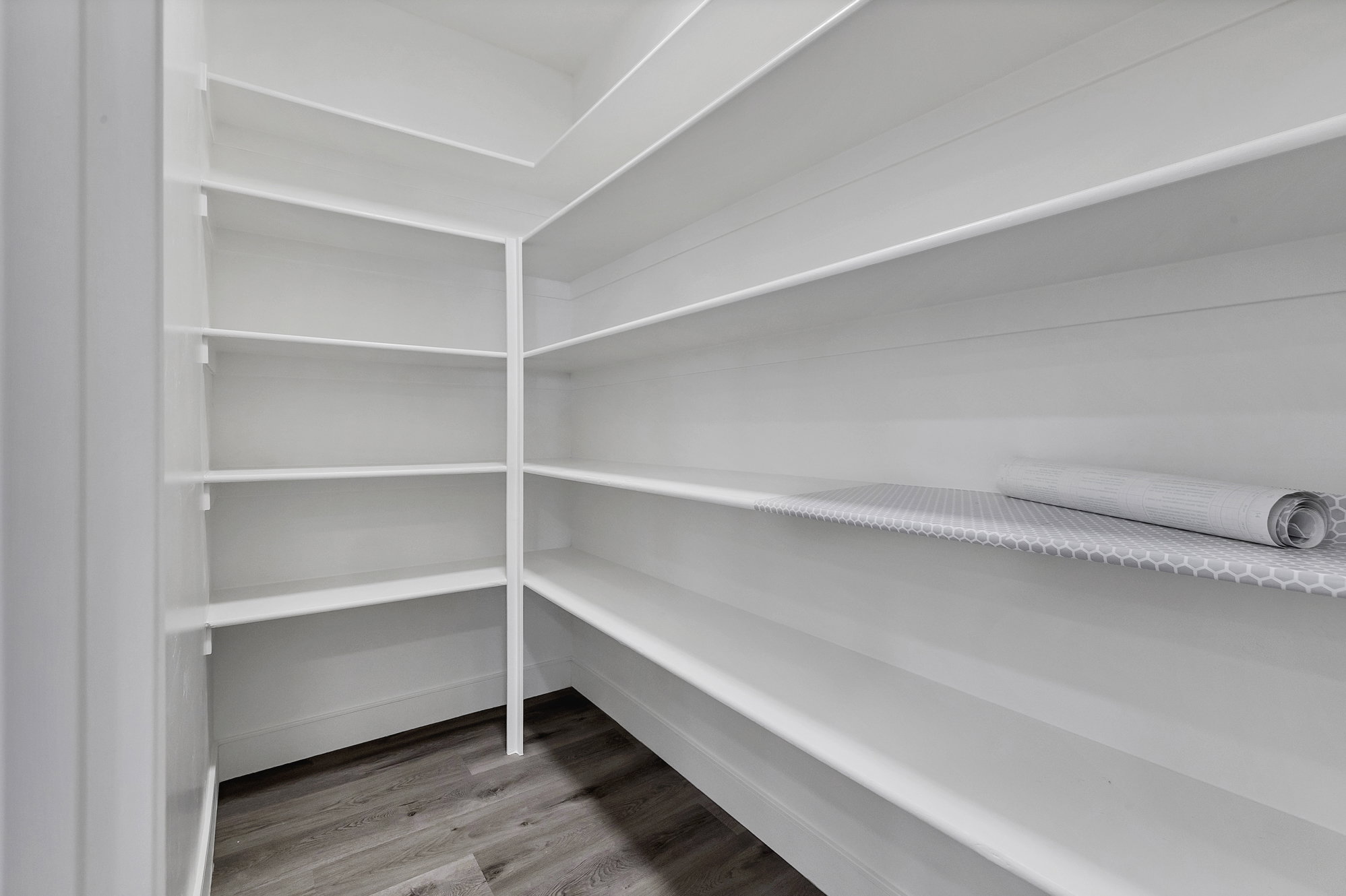 Walk-in pantry featuring extensive white shelving and wood-finish flooring