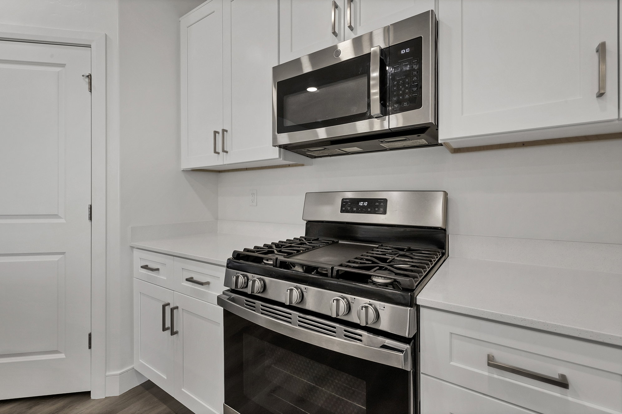 Modern kitchen featuring white shaker cabinetry, stainless steel gas range, stainless steel microwave, light-toned countertops, and wood-finish flooring