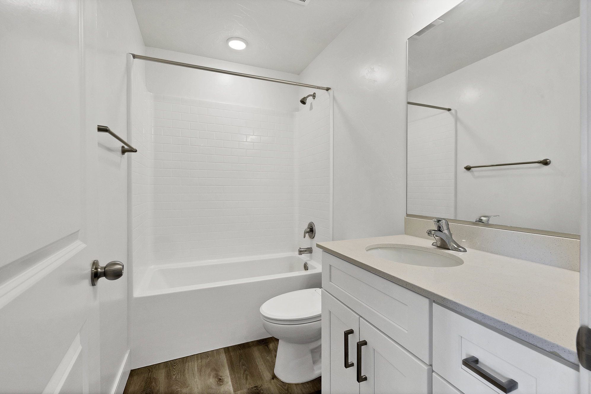 Bathroom featuring a white subway tile tub surround, wood-finish flooring, white vanity with stone-look countertop, and a large wall-mounted mirror