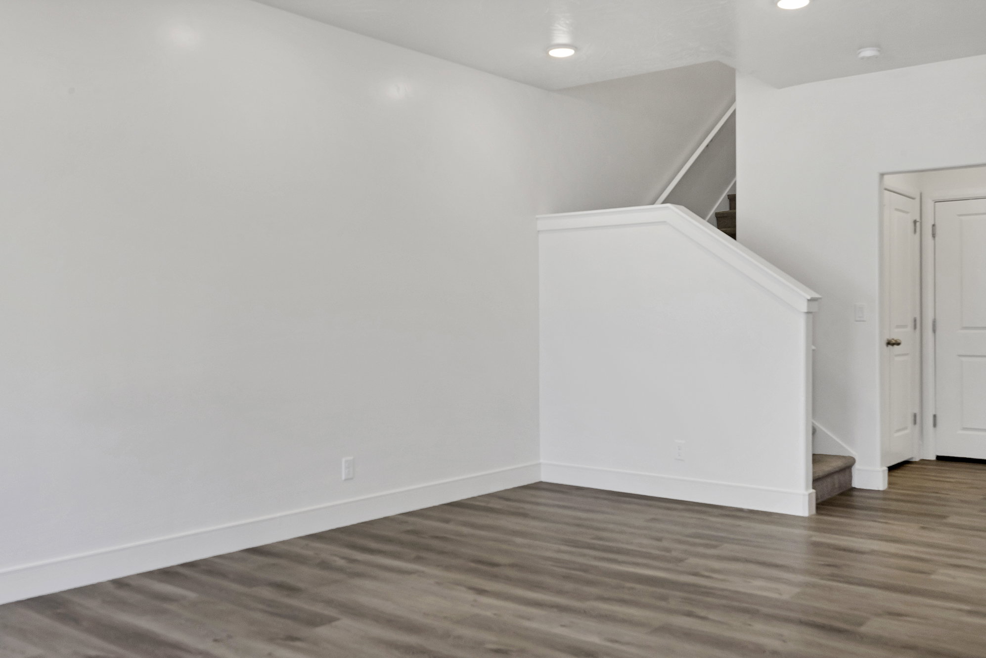 Living area featuring contemporary wood-finish flooring, recessed lighting, and a staircase with white balustrade and carpeted treads