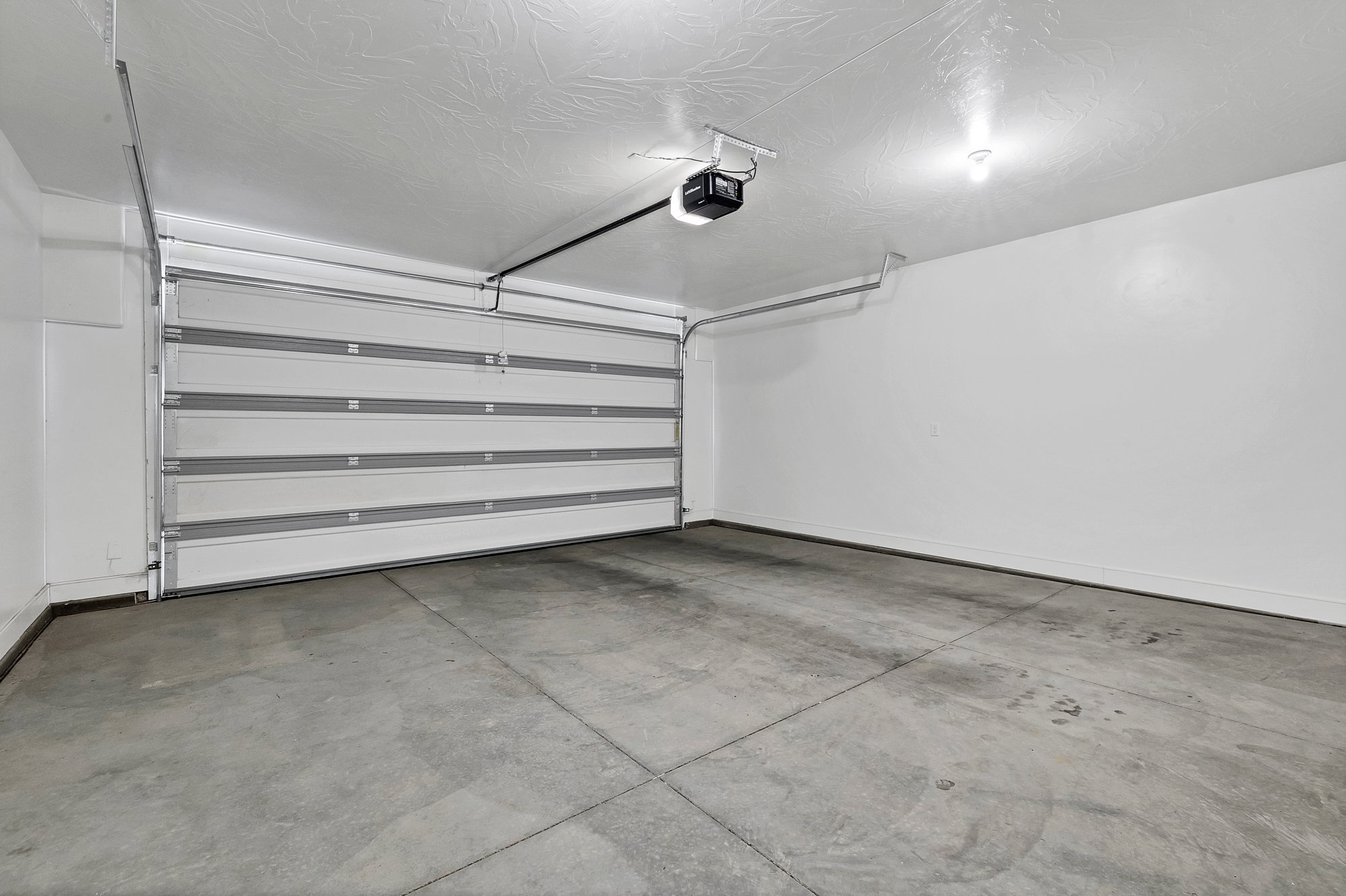 Spacious garage featuring a sectional overhead door with automatic opener, concrete flooring, and overhead lighting