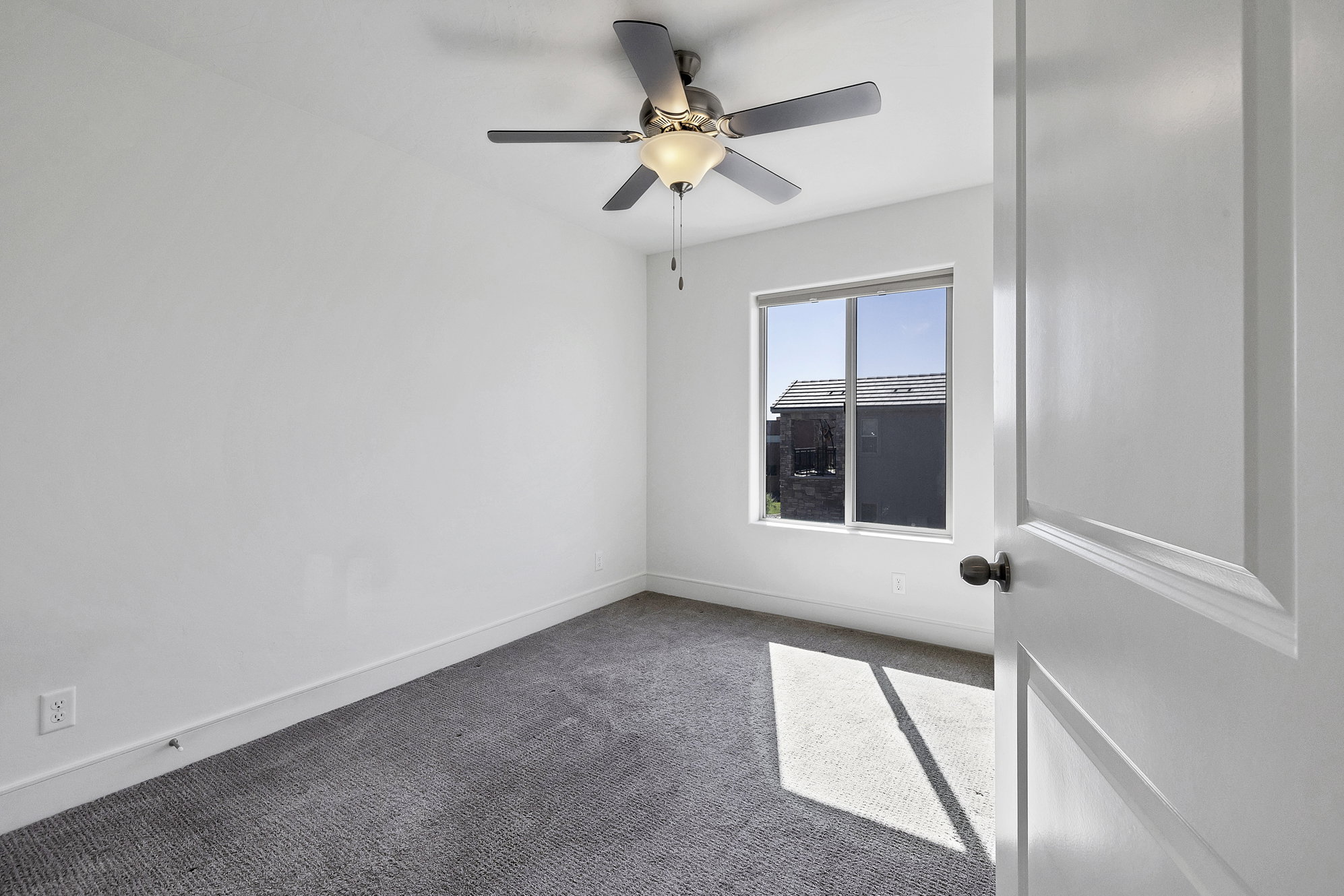 Carpeted room featuring a ceiling fan with integrated lighting, a window, and a white interior door with dark hardware