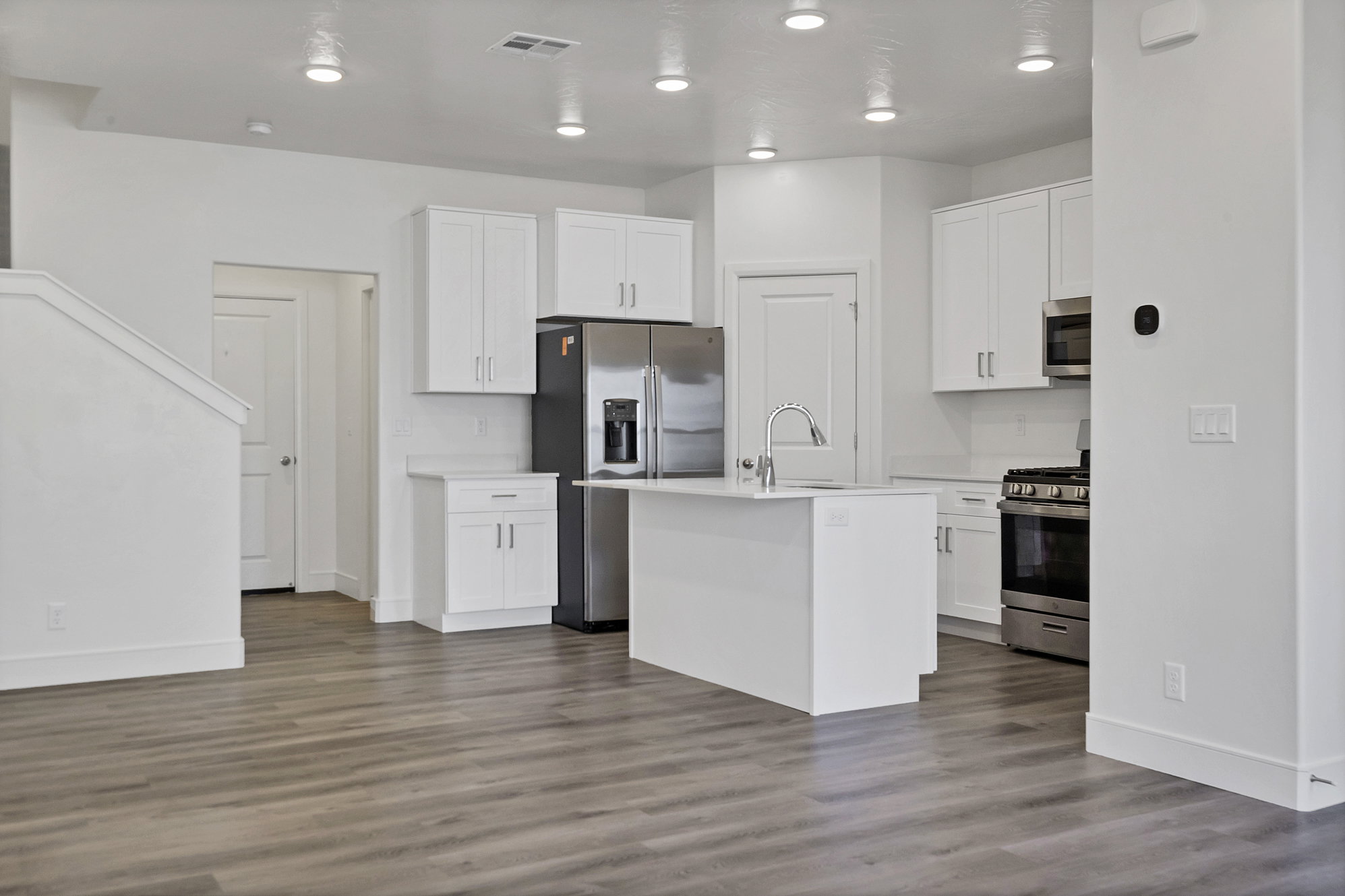 Open-concept kitchen featuring white cabinetry, stainless steel appliances, a central island with sink, and wood-finish flooring