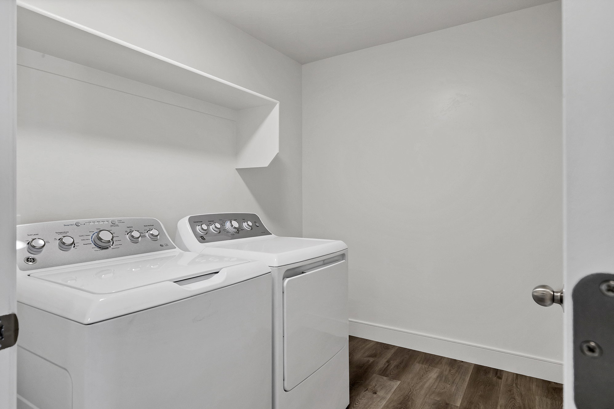 Dedicated laundry area featuring a washer and dryer, wood-finish flooring, white walls, and a built-in storage shelf