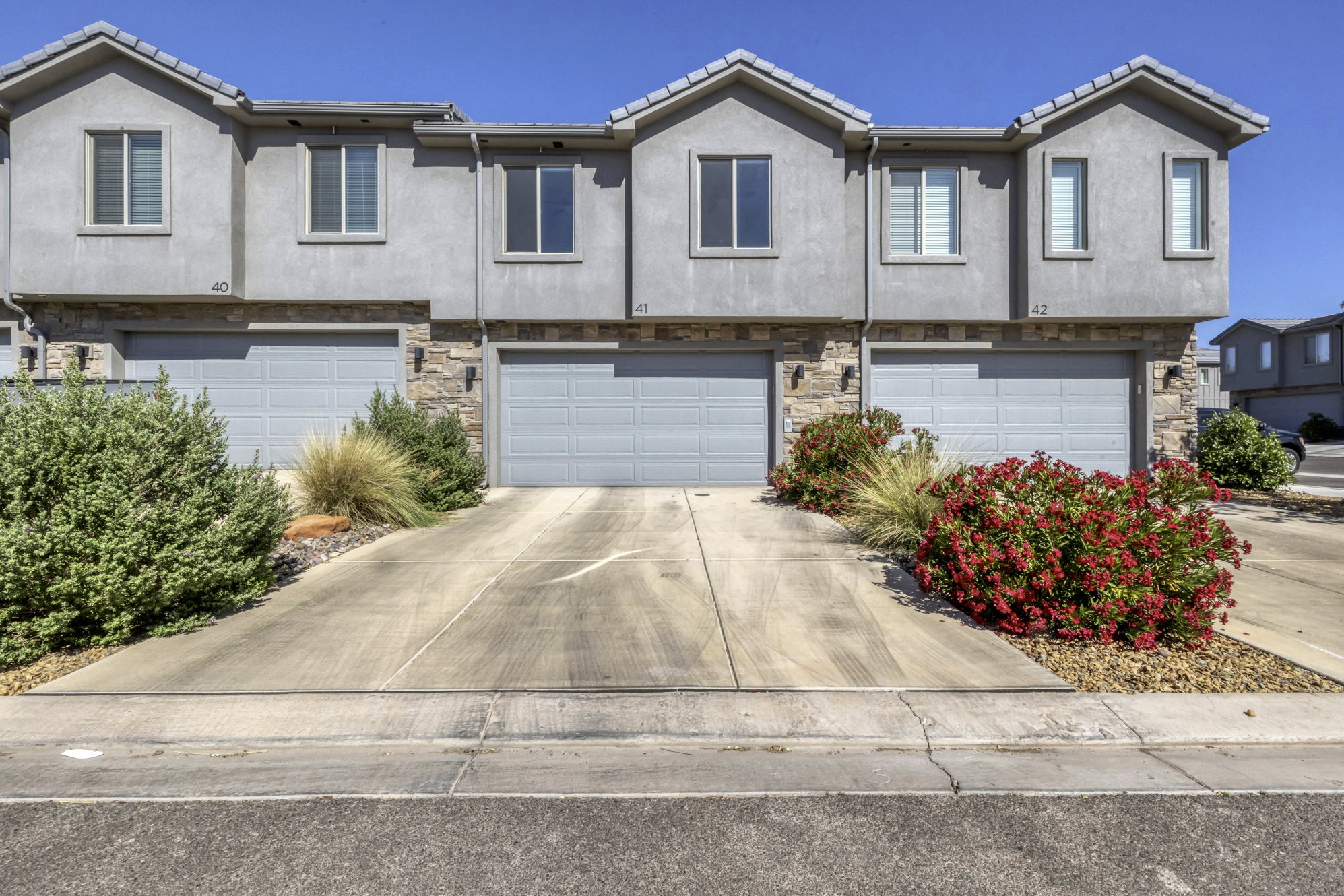 Stucco exterior townhome featuring stone accents and individual garage bays