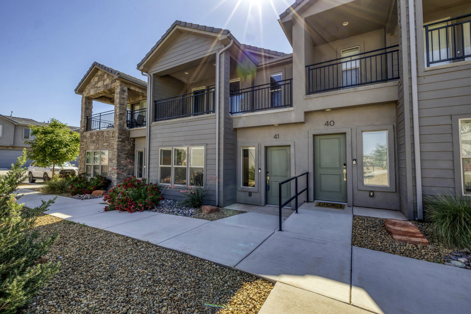Contemporary facade featuring stone accents, multiple balconies with black railings, and a gravel and concrete entryway
