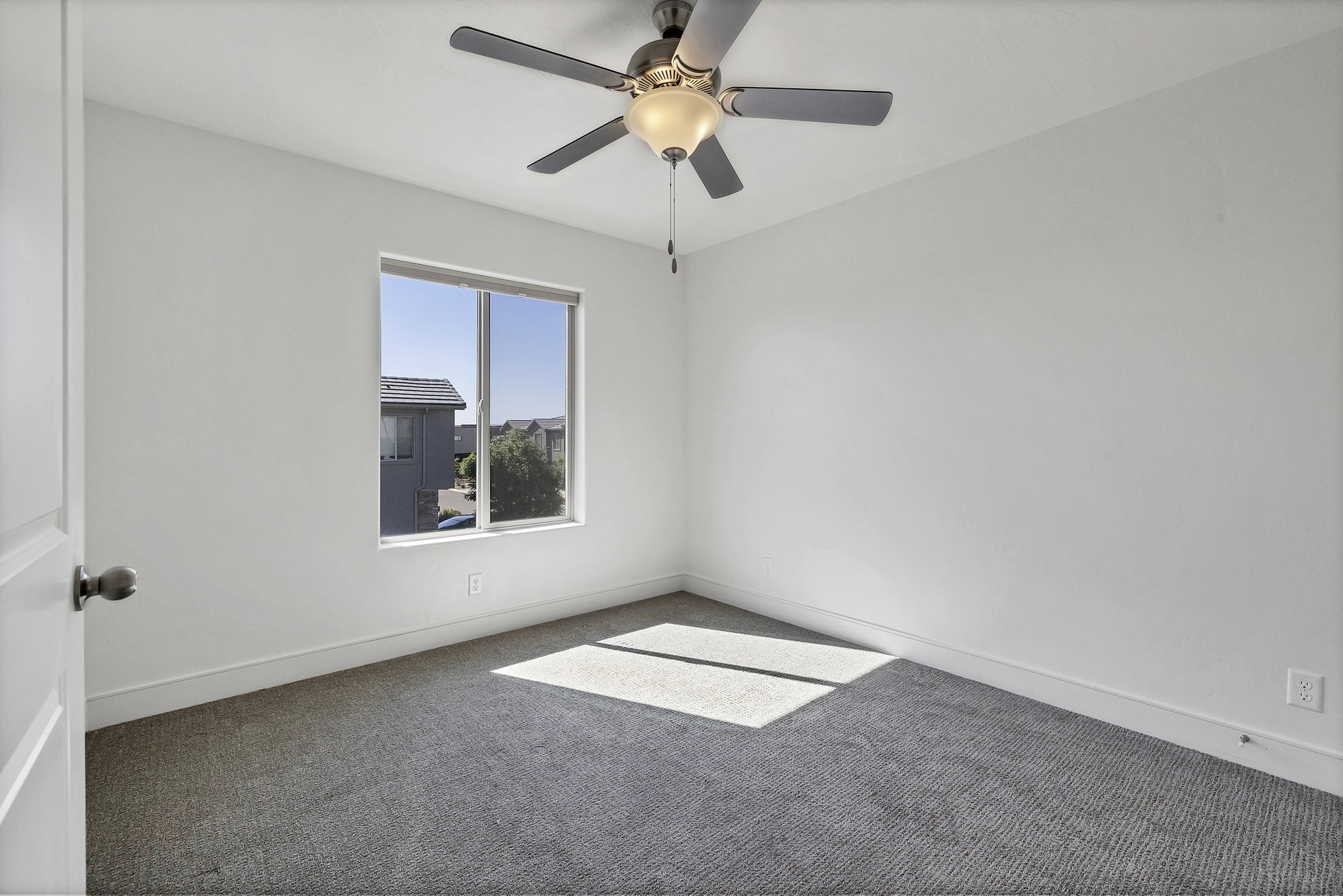 Neutral toned room featuring a single window, a ceiling fan with integrated lighting, white walls, gray carpeting, and white baseboards