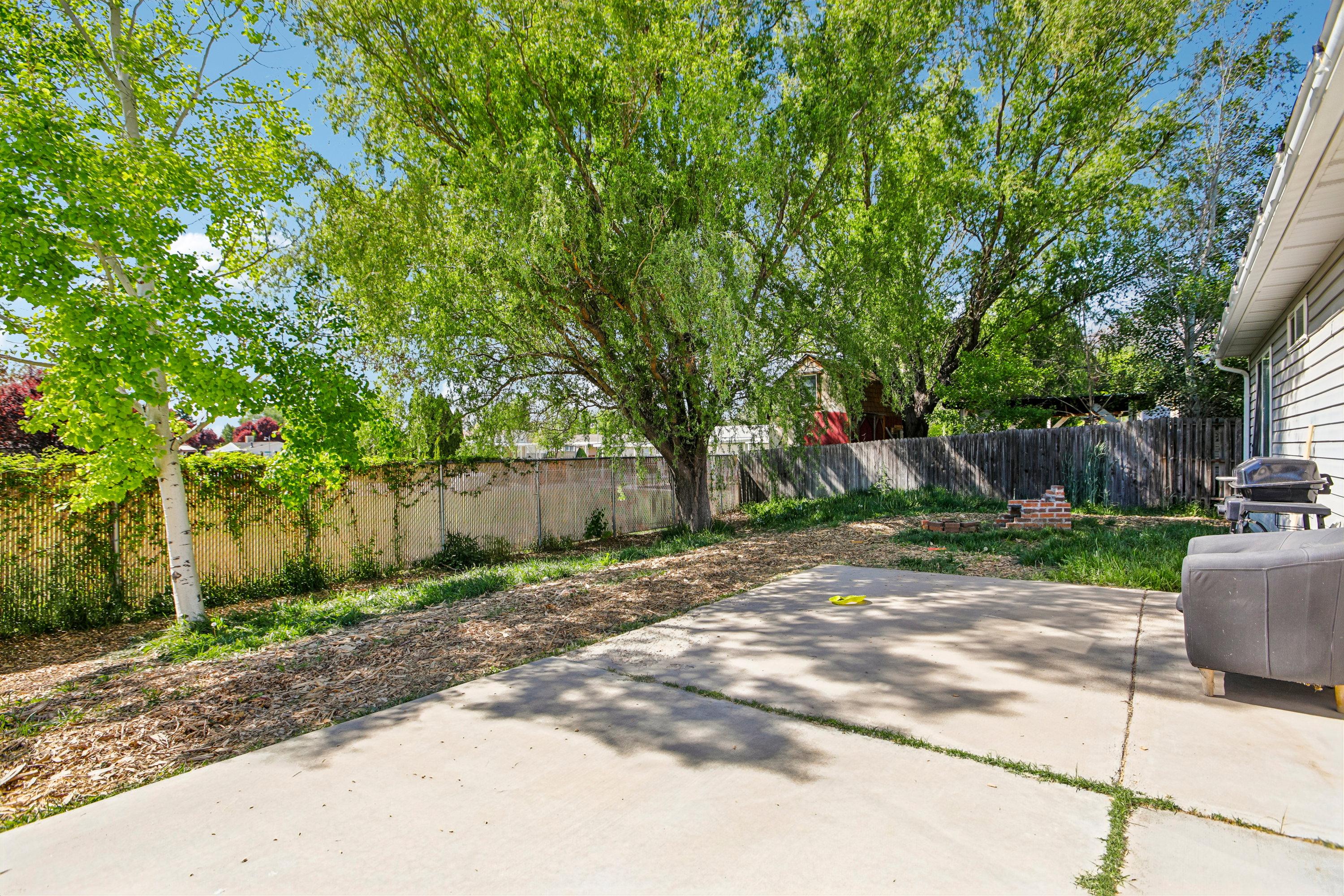 Spacious backyard featuring a concrete patio, mature trees, and a privacy fence