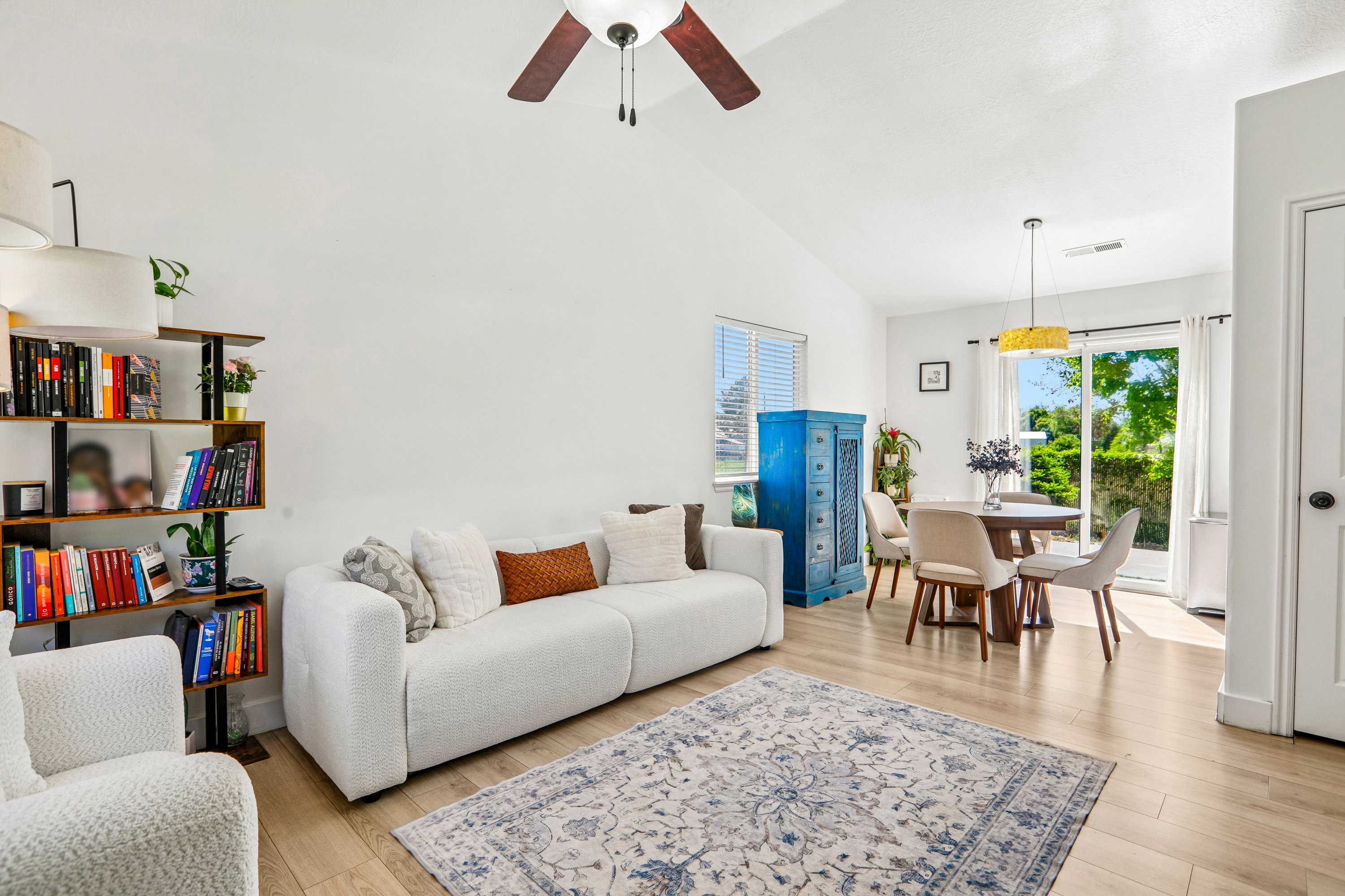 Vaulted ceiling living area featuring wood-finish flooring, a contemporary ceiling fan, and a built-in bookshelf