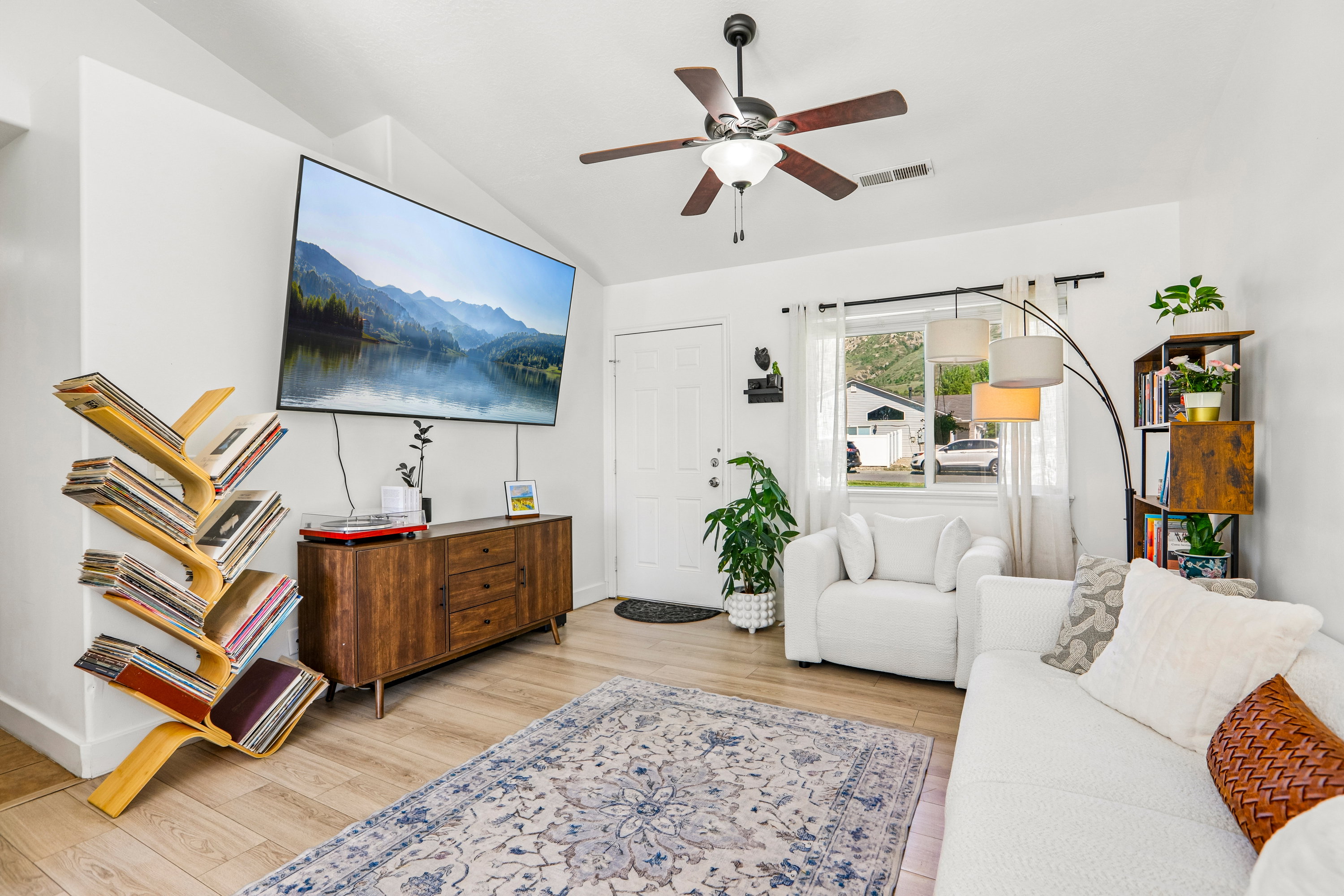 Bright living space featuring wood-finish flooring, a ceiling fan with integrated lighting, and a white entry door