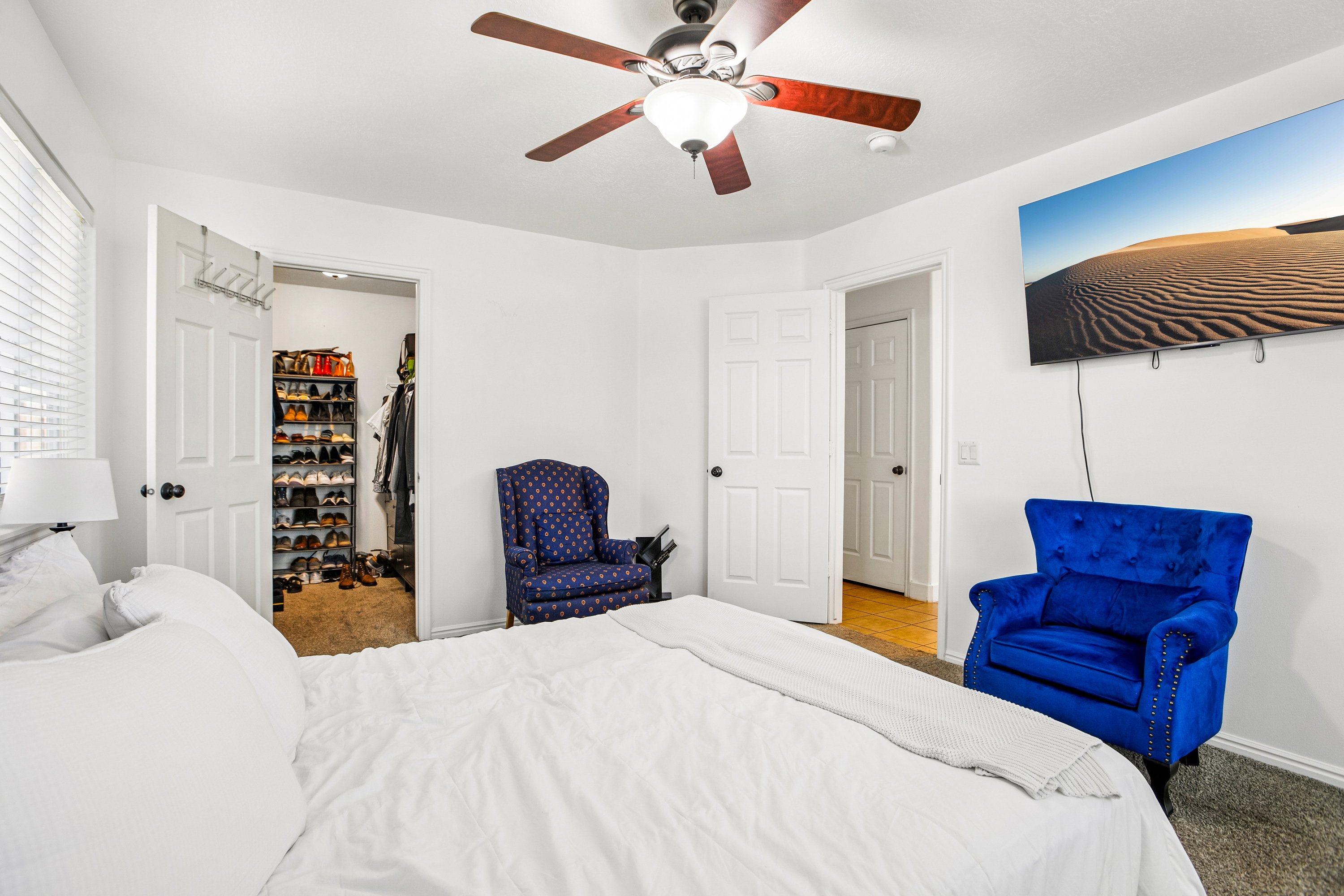 White-painted interior room featuring a ceiling fan with integrated lighting, wood-finish flooring visible through an open doorway, and a built-in closet with shelving