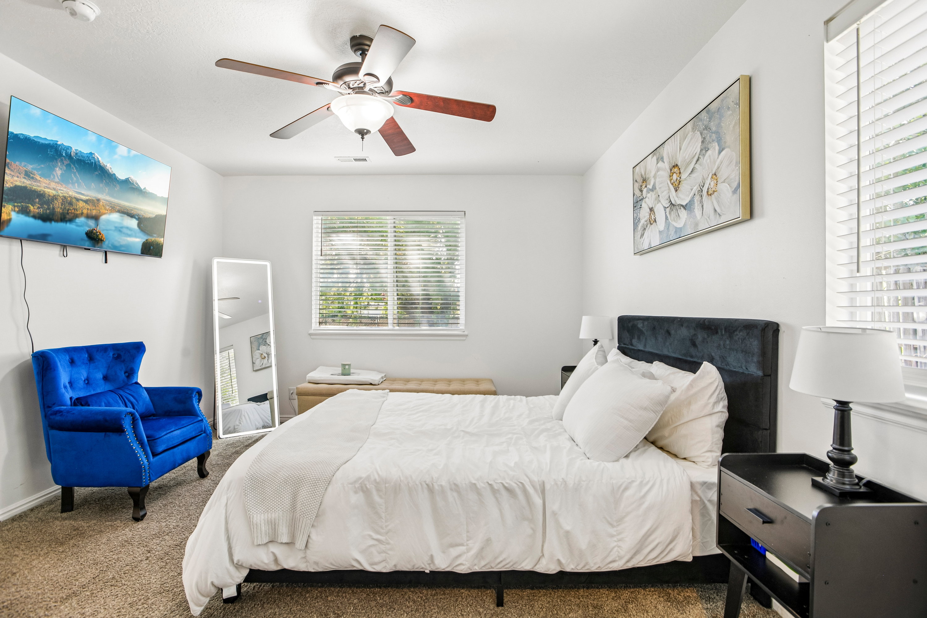 Spacious bedroom featuring a ceiling fan with light fixture, window with horizontal blinds, and warm carpet flooring