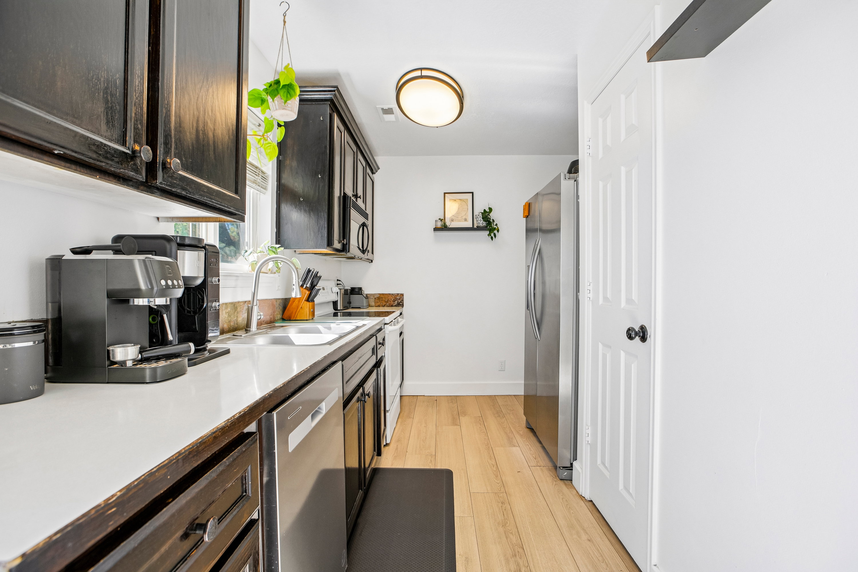 Kitchen featuring dark wood-finish cabinetry, light-toned countertops, a stainless steel sink with a gooseneck faucet, and light wood-finish flooring