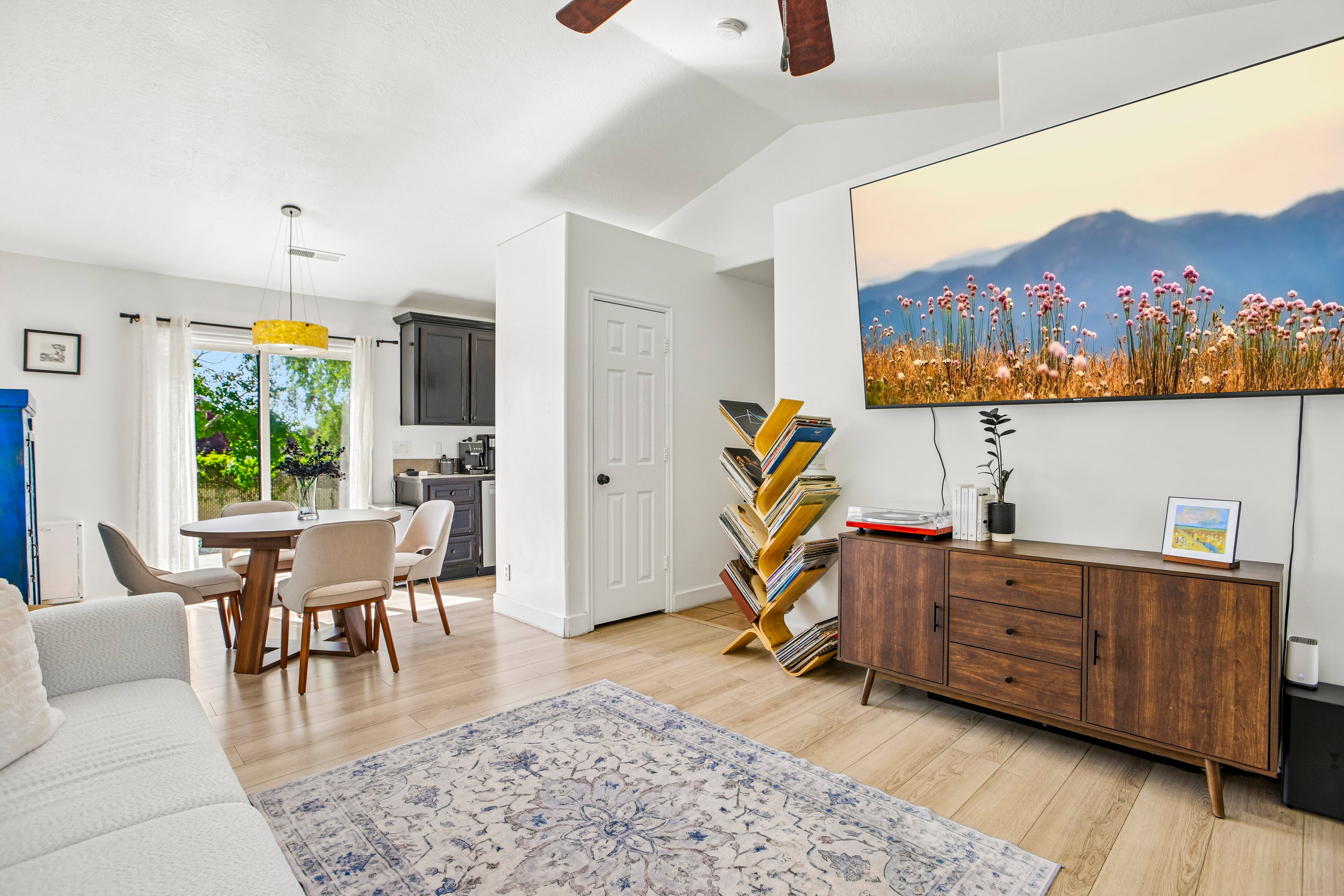 Open-concept living space featuring wood-finish flooring, vaulted ceilings, a ceiling fan, and sliding glass doors providing access to the exterior