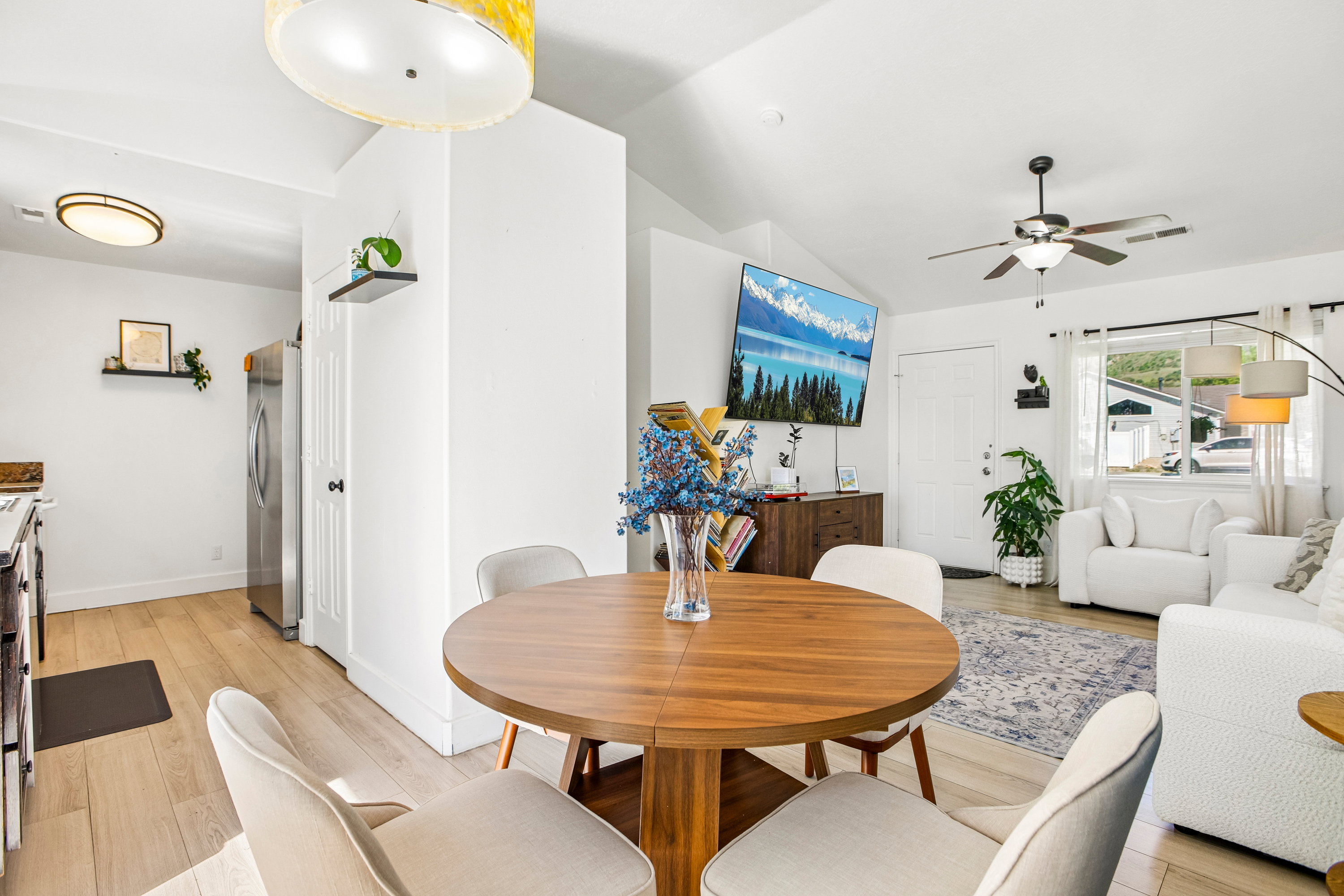 Open-concept living area featuring vaulted ceilings, wood-finish flooring, a contemporary ceiling fan, and a light-filled window