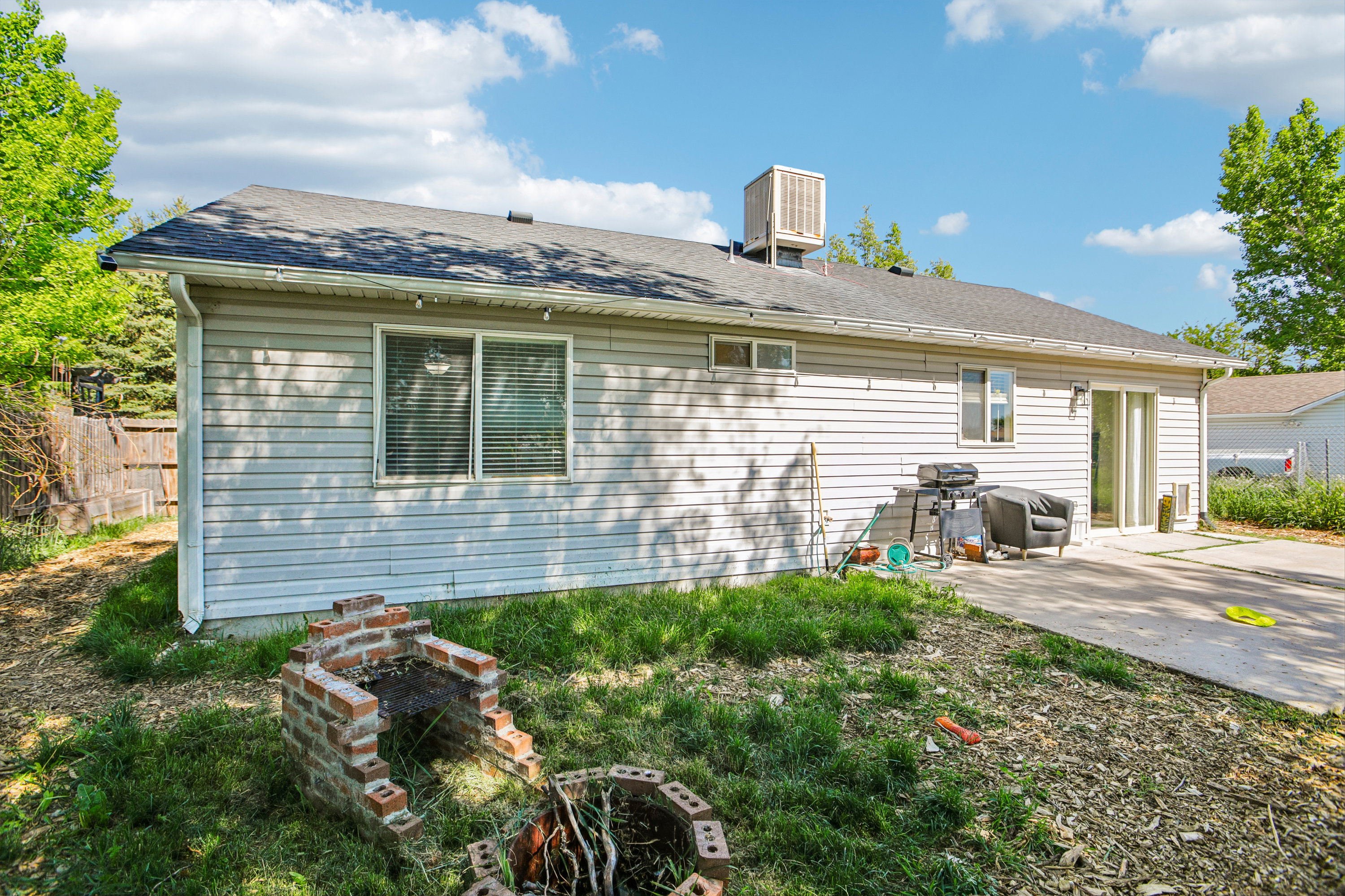 Rear exterior featuring light-colored siding, a dark shingle roof, and a built-in evaporative cooler