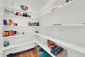Spacious pantry featuring multiple tiers of white shelving, wood-finish flooring, and ample storage capacity