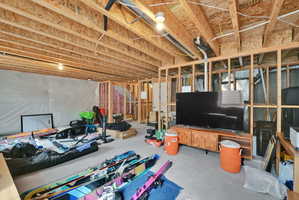 Unfinished basement featuring exposed wood framing, concrete flooring, and an open ceiling with visible joists and electrical conduit