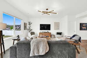 Bright living area featuring a large window, a modern linear chandelier, recessed lighting, white walls, and wood-finish flooring