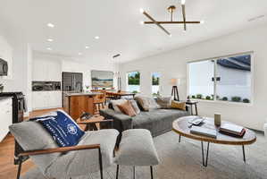 Open-concept living area featuring wood-finish flooring, a contemporary linear chandelier, recessed lighting, and a large window
