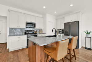 Kitchen featuring white shaker cabinetry, stainless steel appliances, a grey tile backsplash, granite countertops, and wood-finish flooring