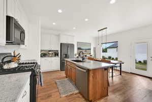 Open-concept kitchen featuring wood-finish flooring, white cabinetry, a large kitchen island with a light-colored countertop, stainless steel appliances, and recessed lighting