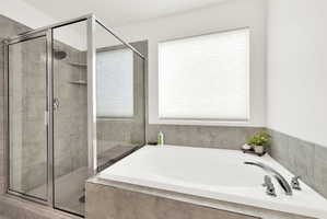 Corner soaking tub with chrome fixtures, glass-enclosed shower, tiled walls, hexagon floor tile, and a privacy window blind
