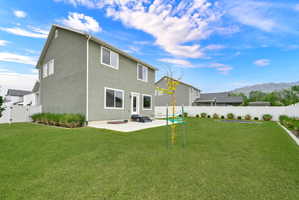 Expansive lawn with a concrete patio, mature landscaping, and a white privacy fence