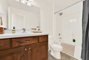 Bathroom featuring a wood-finish vanity with a light-toned countertop, an integrated sink, a large wall-mounted mirror, and a white bathtub with shower functionality