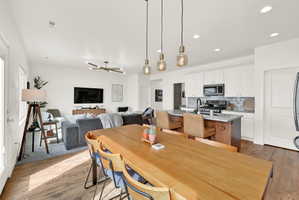 Open-concept living space featuring wood-finish flooring, a contemporary dining table with pendant lighting, a kitchen island with seating, white cabinetry, and recessed lighting