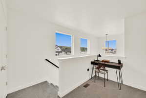 Bright upper-level landing featuring three windows, white walls, and gray carpet