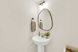Pedestal sink with chrome faucet, complemented by an irregular-shaped mirror with a dark frame