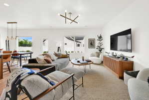 Open-concept living area featuring light wood-finish flooring, white walls, and a modern linear chandelier