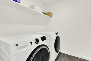 Dedicated laundry area featuring a front-loading washer and dryer, tile flooring, and integrated wall shelving