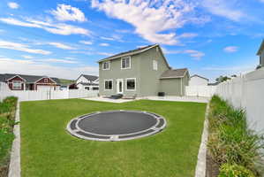 Expansive green lawn with an in-ground trampoline, bordered by a white vinyl privacy fence and a planted bed