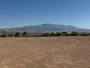Expansive vacant lot featuring a gravel surface, mature palm trees, distant mountainous terrain, and surrounding properties