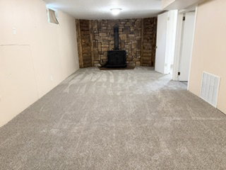 Spacious room featuring new carpeting, a stone-accented wall, and a black wood-burning stove and brand new carpet as of June 26