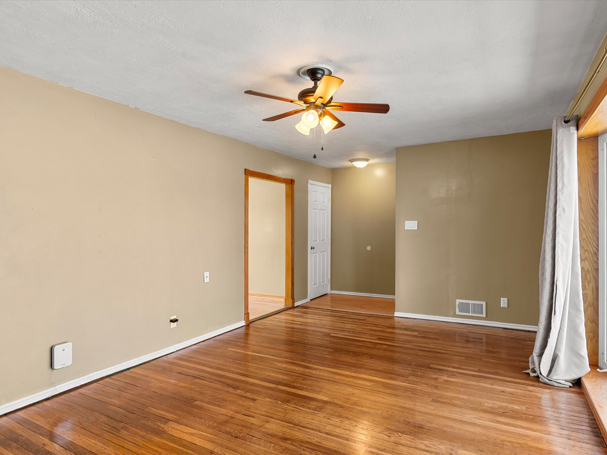 Spacious room featuring wood-finish flooring, light tan walls, and white trim