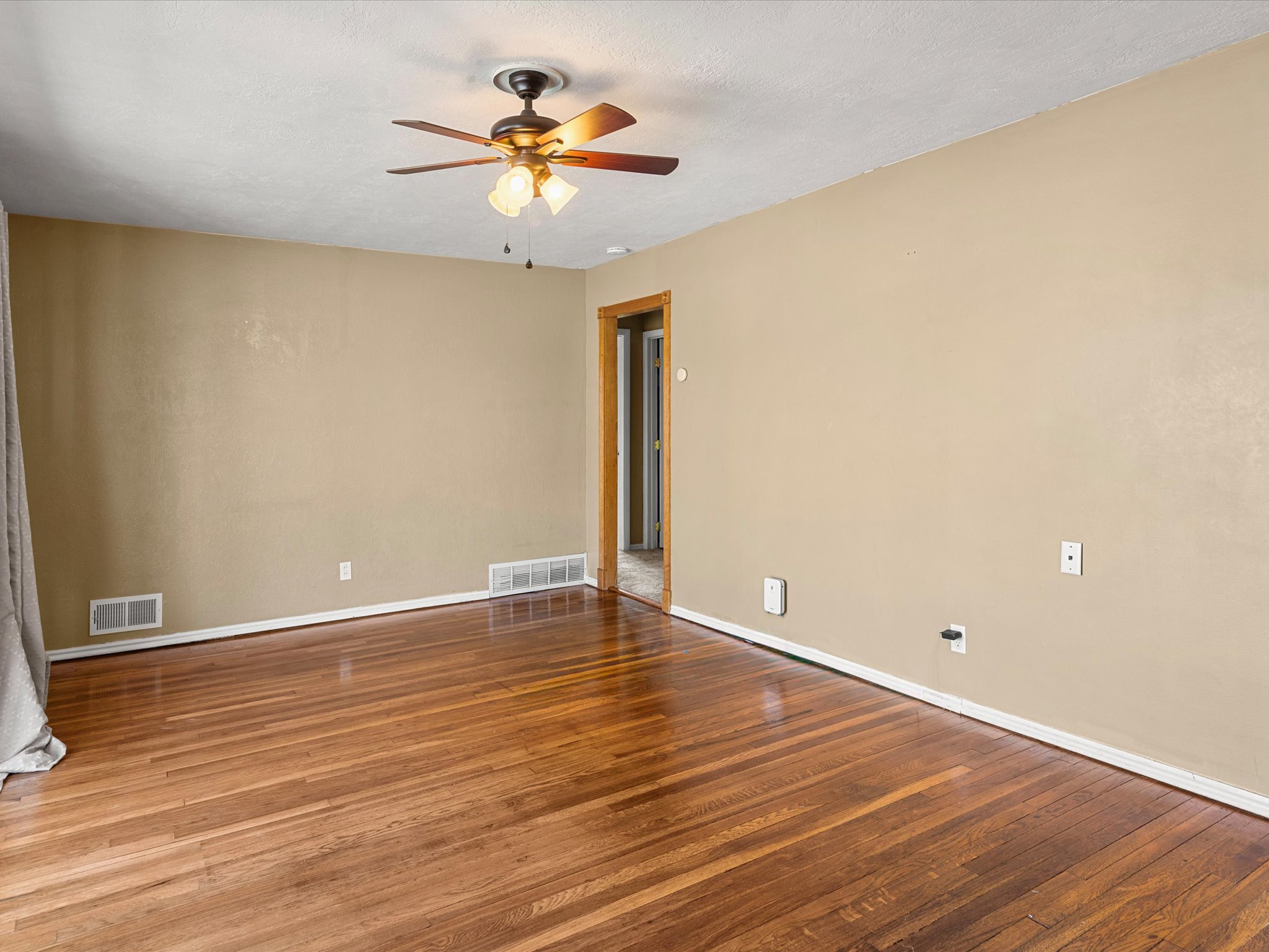 Room featuring rich wood-finish flooring, light tan walls, white baseboards, and a bronze ceiling fan with integrated lighting