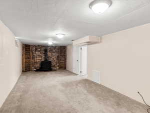 Spacious room featuring neutral carpet flooring and a prominent stone accent wall with a built-in black wood-burning stove