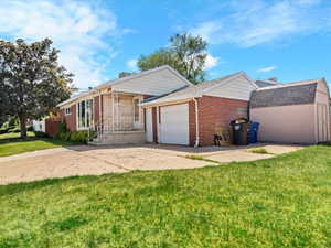 Brick exterior featuring a covered front porch with white railings, an attached single-car garage, an additional detached shed, and a concrete driveway