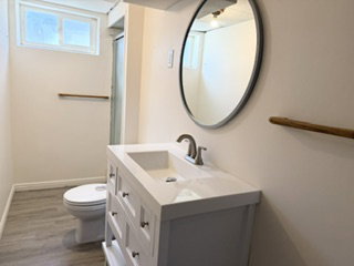 Modern bathroom featuring a white vanity with integrated sink, brushed nickel faucet, and a round wall-mounted mirror