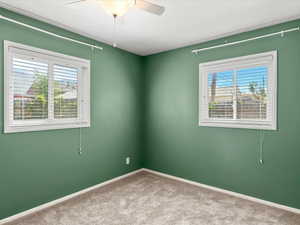 Carpeted interior space featuring two windows with horizontal blinds, a ceiling fan with light fixture, and crown molding