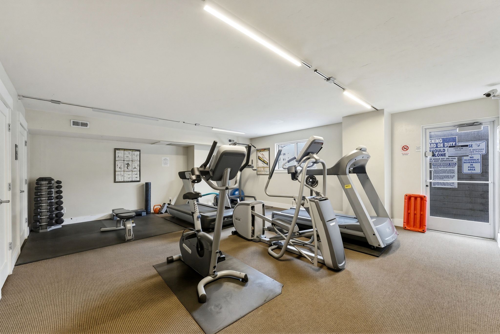 Dedicated fitness room featuring cardio machines, weight racks, and a rubber mat flooring section
