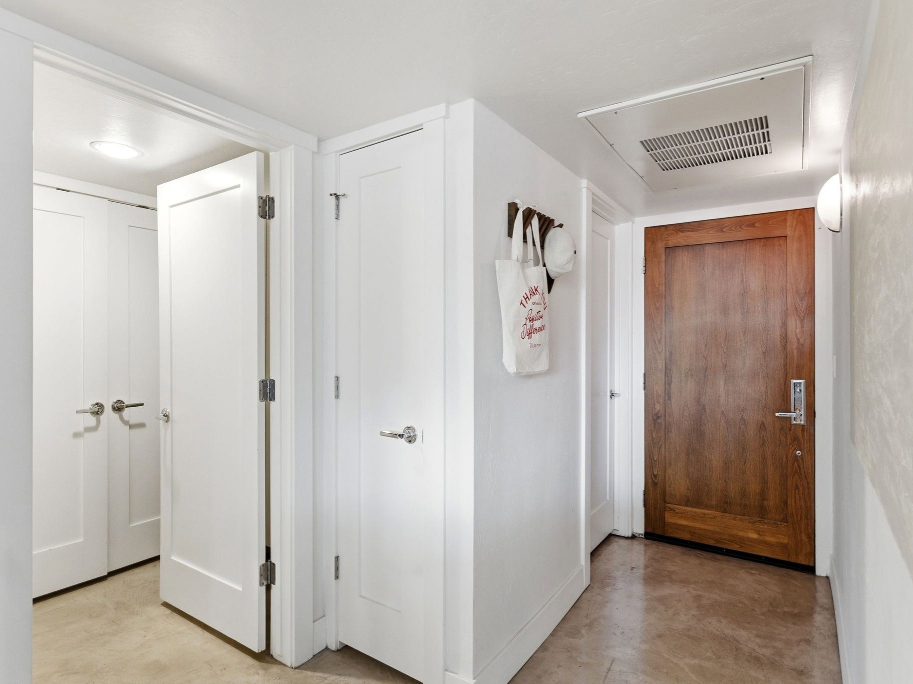 Hallway featuring a natural wood-finish door with brushed nickel hardware, bright white interior doors, recessed lighting, and a wall-mounted light fixture