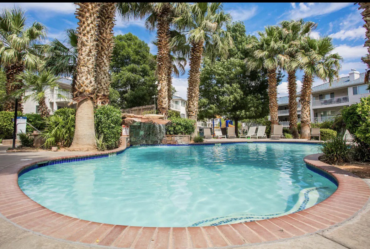 Community swimming pool with a decorative waterfall feature, surrounded by mature palm trees and lush landscaping