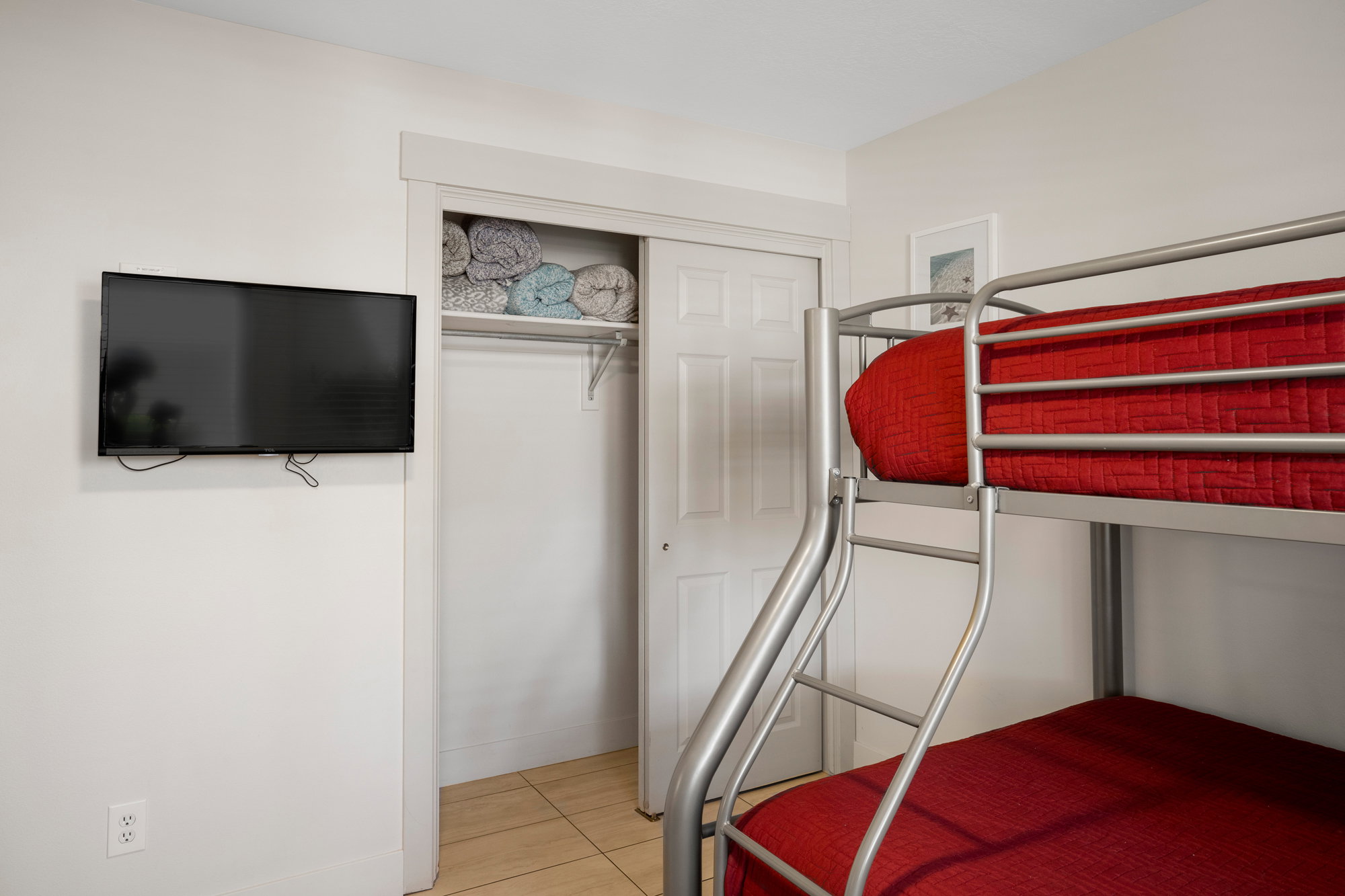 Room featuring a built-in metal bunk bed, wall-mounted television, and a closet with bifold doors